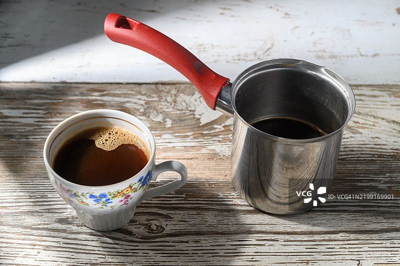 在晨光中，享受一杯新鲜冲泡的咖啡，放在质朴的木桌上。图片素材