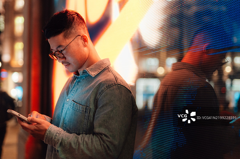 年轻的亚洲男子在夜晚的城市中使用智能手机图片素材