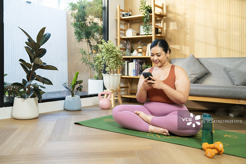在家练习瑜伽的女人微笑着查看她的智能手机图片素材