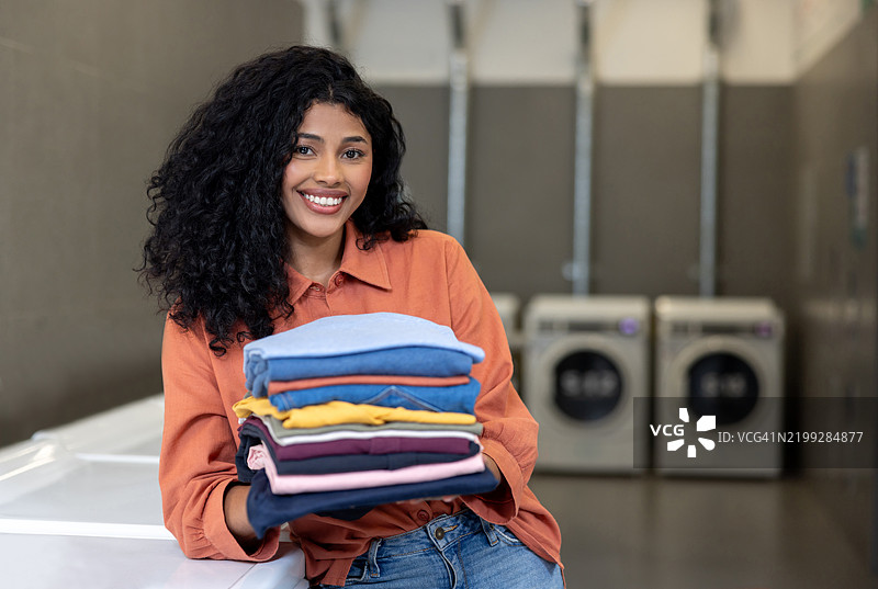 在洗衣店里，快乐的女人手里拿着叠好的衣服的肖像图片素材