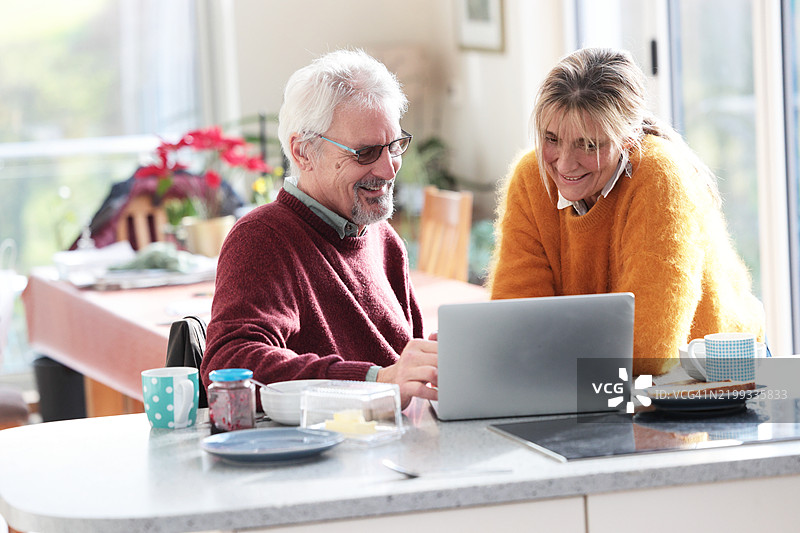 一对情侣在厨房早餐吧台前看着笔记本电脑图片素材