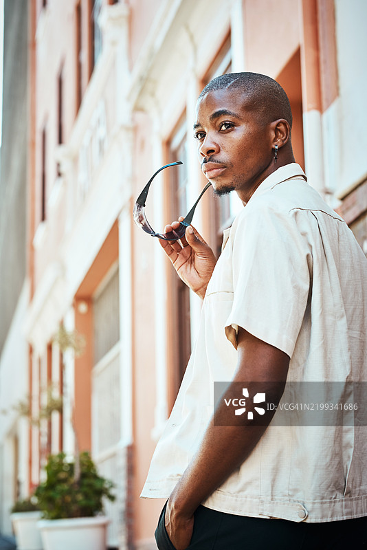 时尚个体在城市街道上手持太阳镜，若有所思地凝视着。图片素材