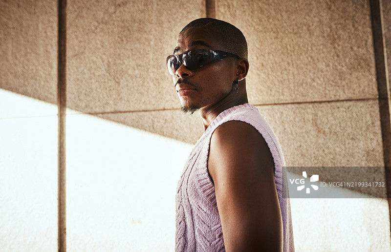 自信的男士戴着时尚的太阳镜和毛衣，站在戏剧性的灯光下图片素材