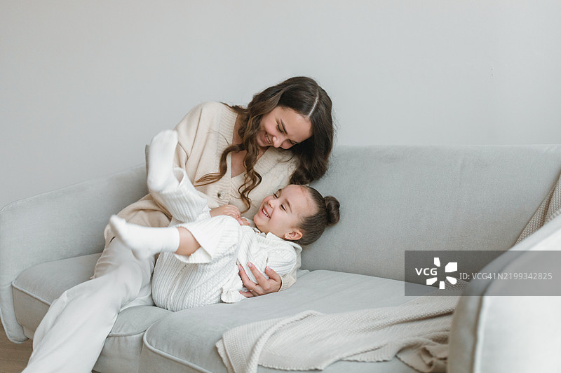 快乐的女人坐在沙发上，给她的小女儿挠痒痒的特写镜头图片素材