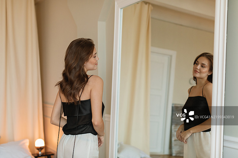 时尚年轻女性站在卧室的镜子前，注视着自己的倒影图片素材