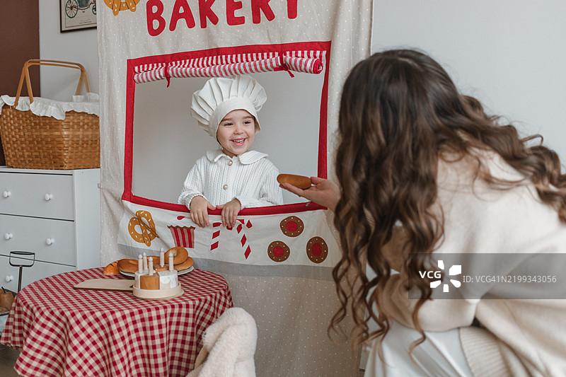 微笑的女孩在面包店假装是糕点师，正看着她的母亲。图片素材