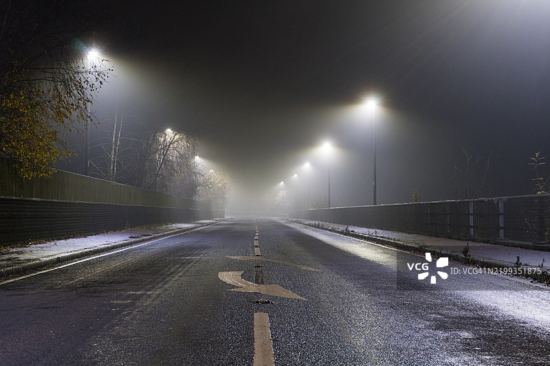 一条笔直的长路，路面上画着箭头。在一个神秘的雾夜。图片素材