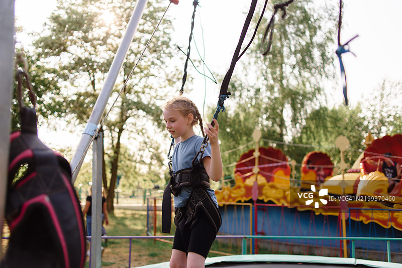 一个女孩在儿童游乐园的蹦床上快乐地跳跃，享受户外乐趣和积极的游戏。图片素材