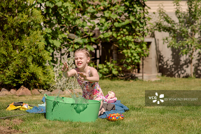 一个小女孩在院子里玩水玩具，享受夏日的炎热。图片素材
