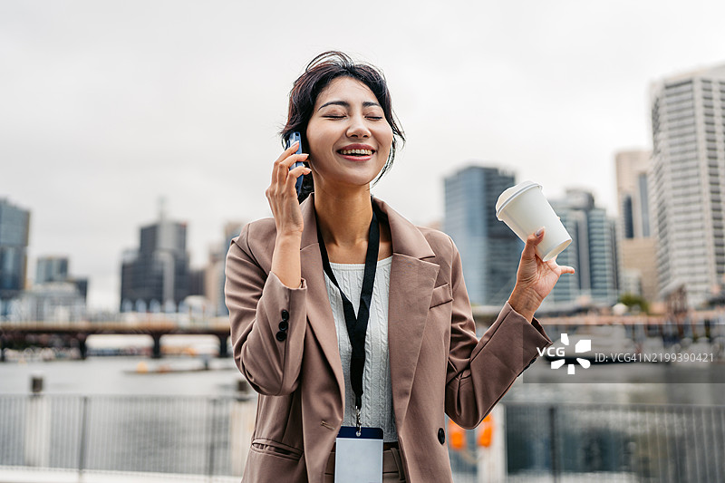 年轻的亚洲女商人在澳大利亚悉尼达令港一边喝外带咖啡一边打电话图片素材