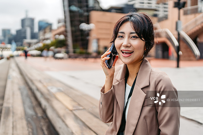 年轻的亚洲女商人在澳大利亚悉尼达令港的码头边坐着打电话图片素材