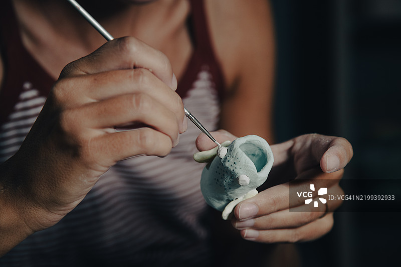 一位女性在陶艺工作室的桌子旁，近距离为陶土鱼上釉。图片素材