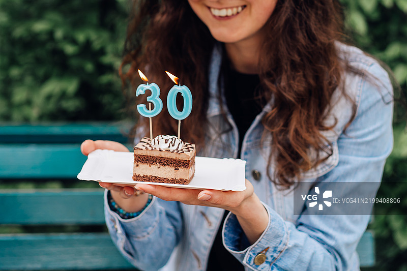 户外一位女性手持30根蜡烛的生日蛋糕图片素材