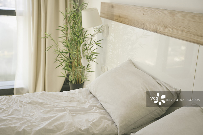 卧室室内细节，米色床单和枕头的床，灯和家居植物图片素材