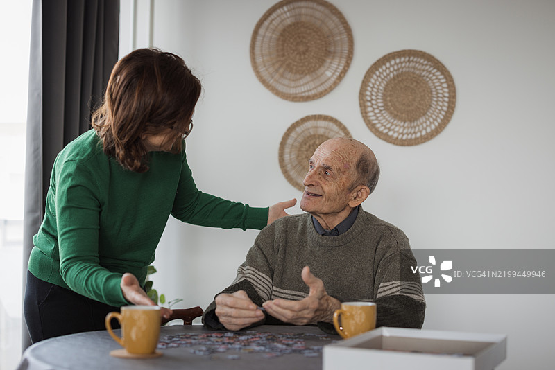 养老院中，志愿者探访一位老人，二人一起玩拼图。图片素材