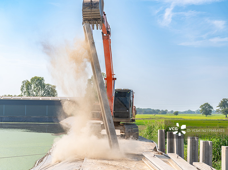 挖掘机正在提升堆积物，周围扬起尘土。图片素材