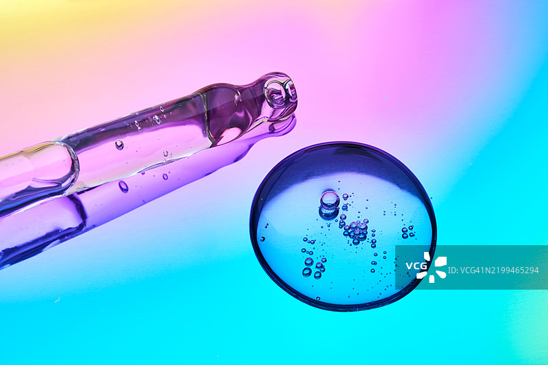 一滴化妆品精华和一个吸管在蓝色和紫色渐变的多彩背景上图片素材