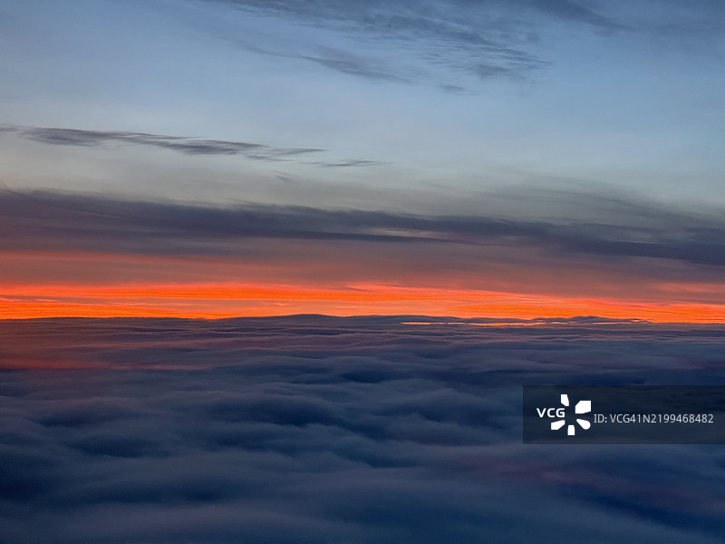明亮的橙色日落天空在云层上方，位于德国黑森州富尔达的Hnfeld，2023年12月。图片素材