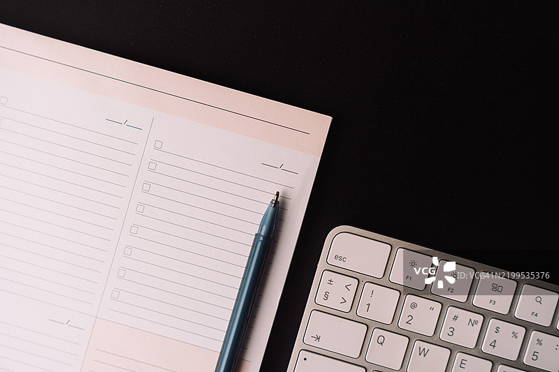 从上方拍摄的桌面记事本照片，黑色背景的键盘图片素材