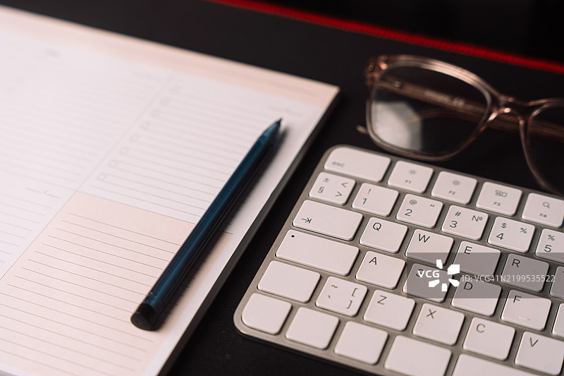 黑色背景下的桌面笔记本、键盘和粉色眼镜图片素材