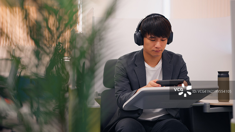 商人在绿色办公空间中戴着耳机放松图片素材
