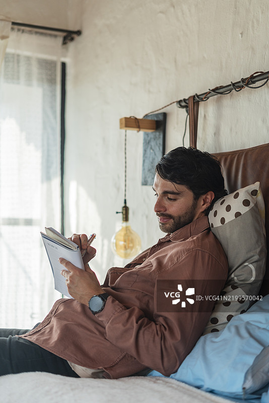 男人在床上休息，放飞想象，思考好点子并将其写下。图片素材