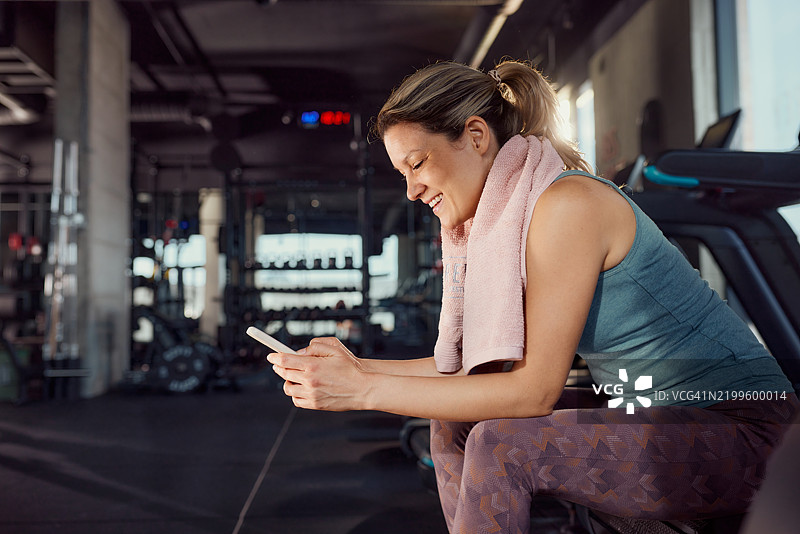 快乐的运动女性在健身房休息时使用手机。图片素材