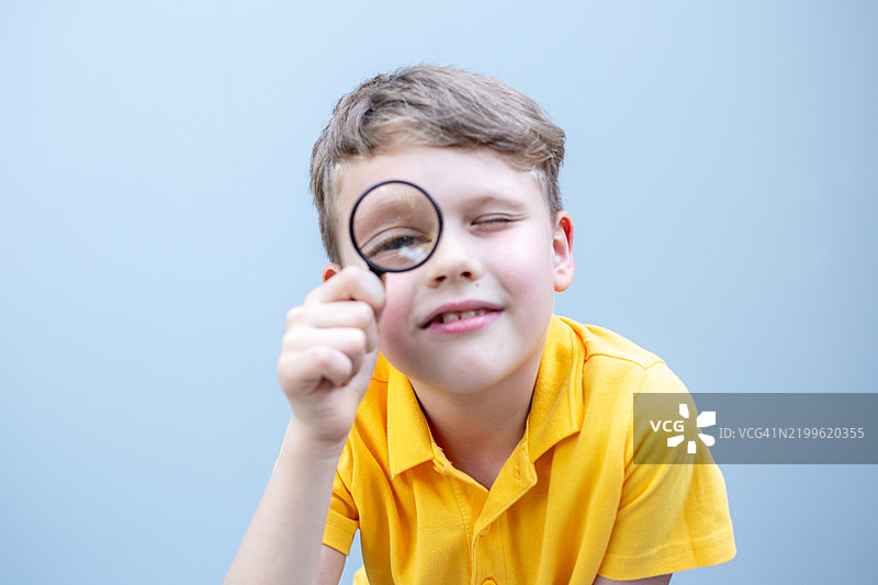 穿着黄色T恤、手持放大镜的可爱男孩摄影，像个侦探。图片素材
