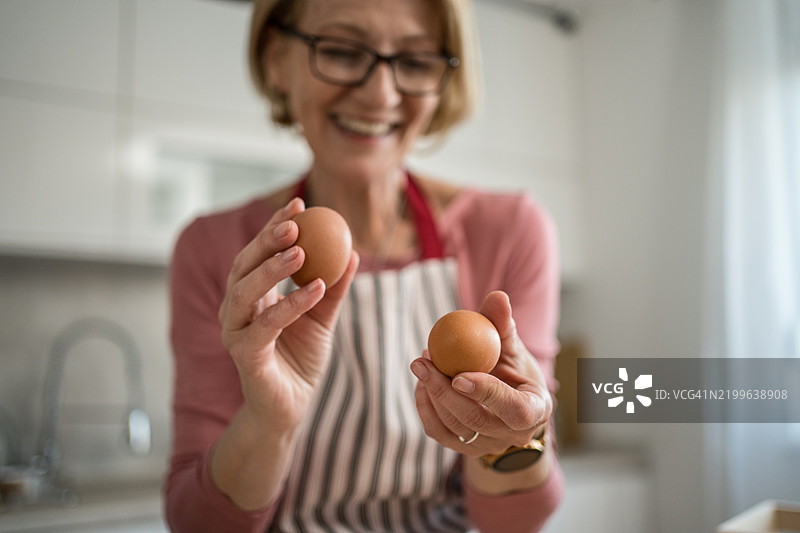 中年女性在现代厨房里微笑着拿着新鲜的鸡蛋图片素材