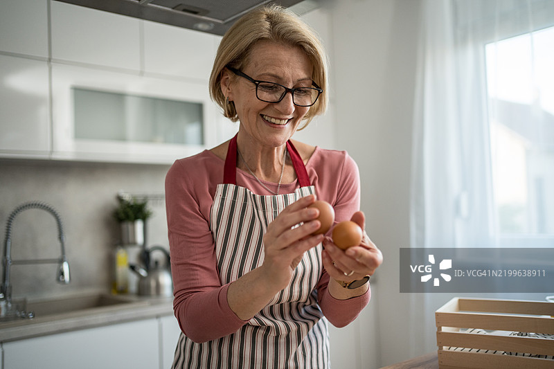 中年女性在现代厨房里微笑着拿着新鲜的鸡蛋图片素材