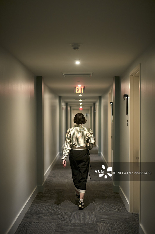穿着条纹衬衫的女人走在昏暗的走廊上，地毯是灰色的，地点：美国佛罗里达州迈阿密图片素材