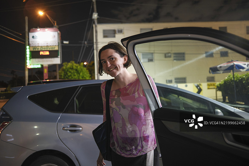 穿着粉色花卉上衣的女性在佛罗里达群岛的城市夜晚微笑着打开车门图片素材