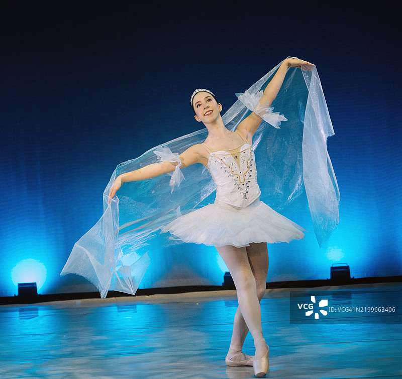 穿着白色芭蕾舞裙的舞者在蓝色灯光下优雅地在舞台上表演。《胡桃夹子》，美国贝恩布里奇岛图片素材
