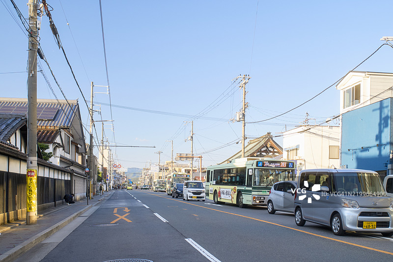 宁静的城市街道，汽车、公交车和传统建筑在晴朗的蓝天下。日本京都图片素材