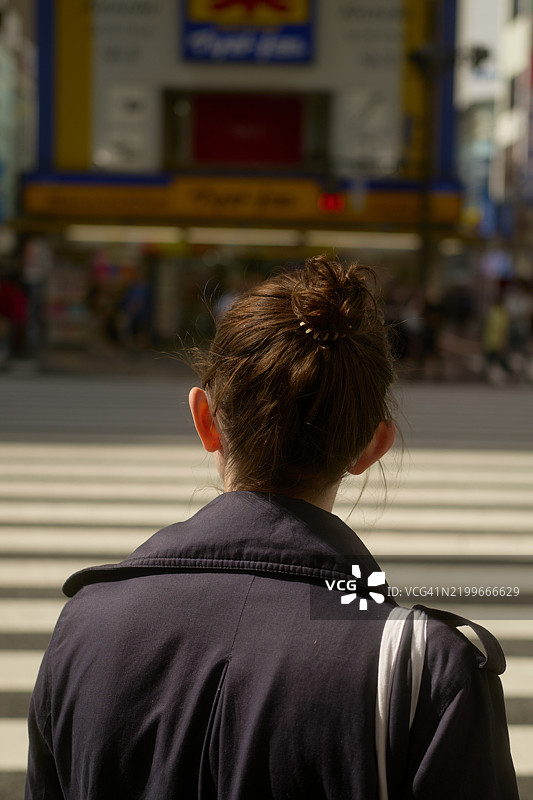 在阳光明媚的日子里，扎着发髻的女性正在东京的城市街道上穿行。图片素材