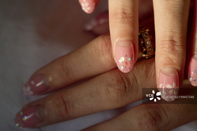 特写镜头展示了手部的粉色花卉美甲，包含精致的设计和一枚金色戒指。日本东京图片素材