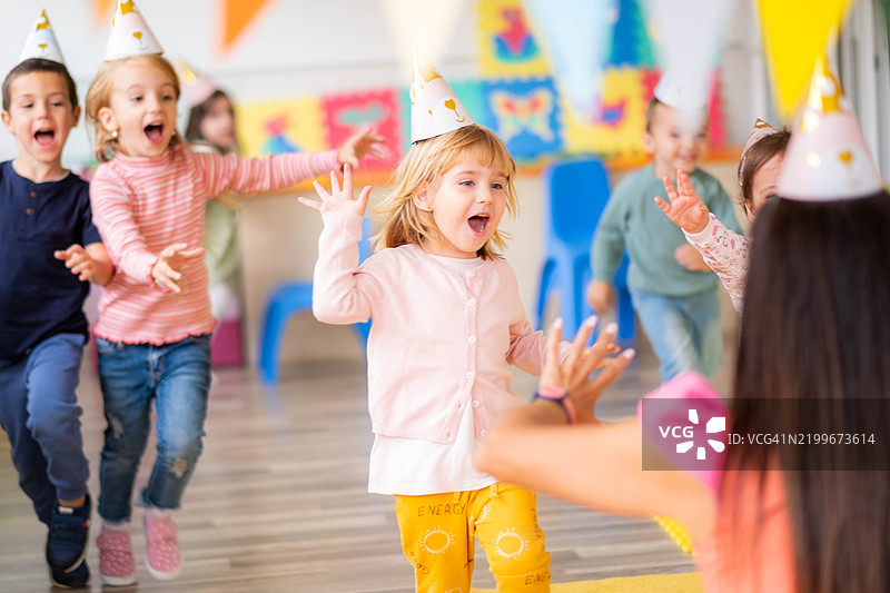 快乐的小朋友们在游乐场庆祝生日，奔跑、玩耍，头上戴着生日帽。图片素材