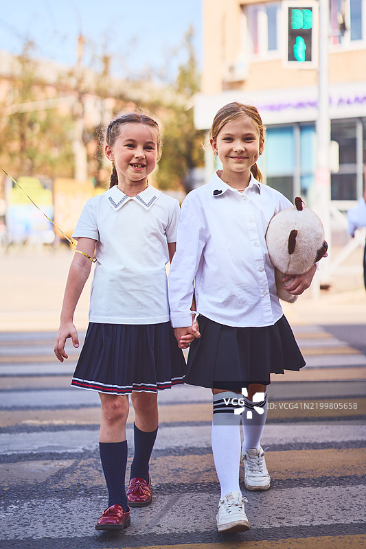 两个年轻的女学生手牵手走过人行横道，回到学校的概念图片素材