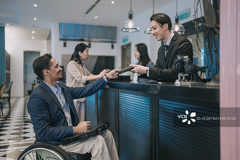 坐在轮椅上的印度商人在酒店前台办理入住，递交护照进行验证。图片素材
