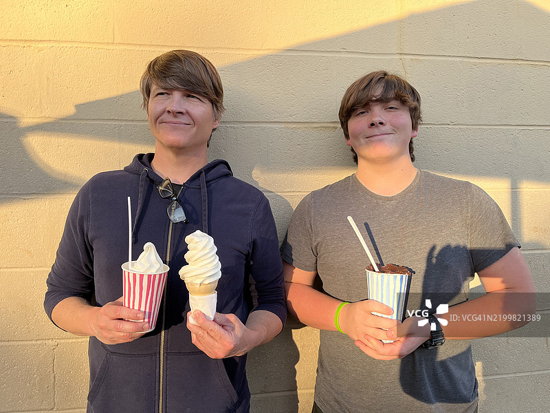 父亲和儿子在路边摊享用软冰淇淋的肖像。图片素材