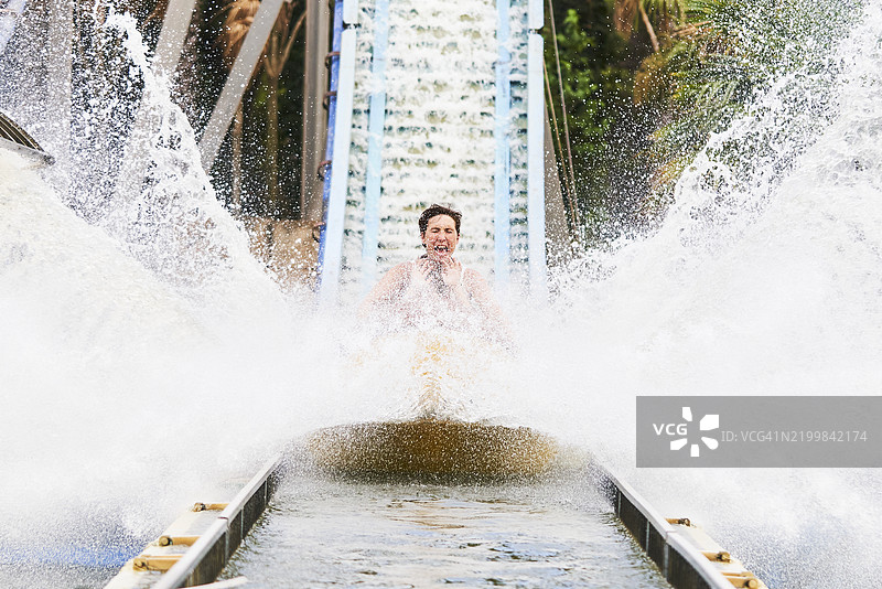 游乐园水滑梯的正面视图，水花四溅，一位女性和孩子们坐在上面，尽情享受乐趣。图片素材