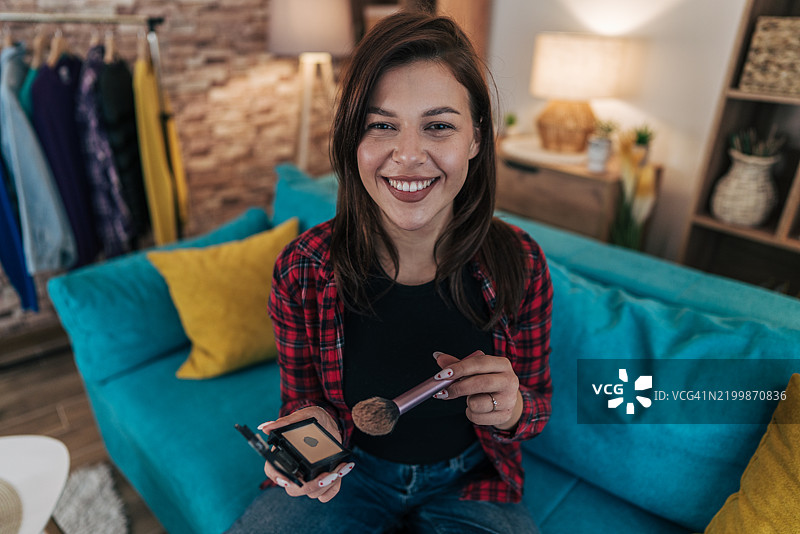 年轻女性在家化妆，面带微笑看向镜头图片素材