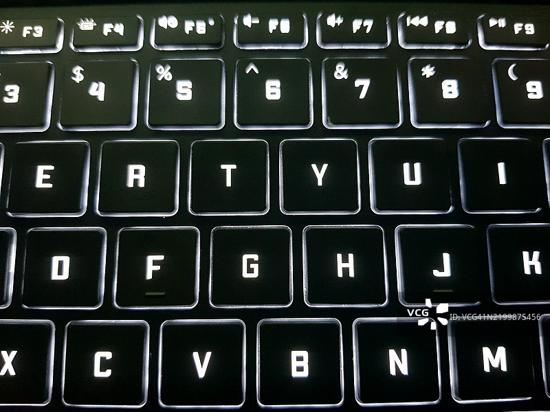 夜间照亮的笔记本电脑或计算机键盘特写。图片素材