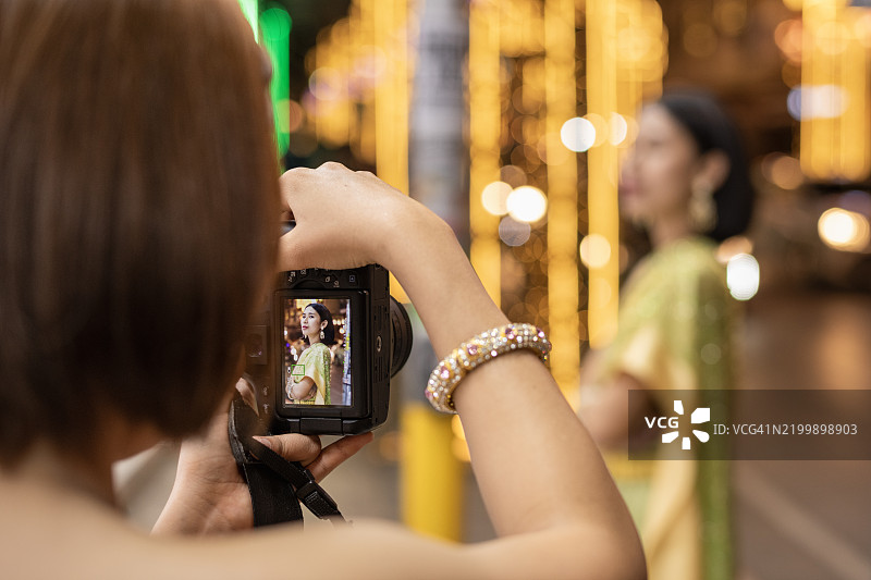 一位年轻女性正在为另一位穿着传统泰国服装的女性拍照图片素材