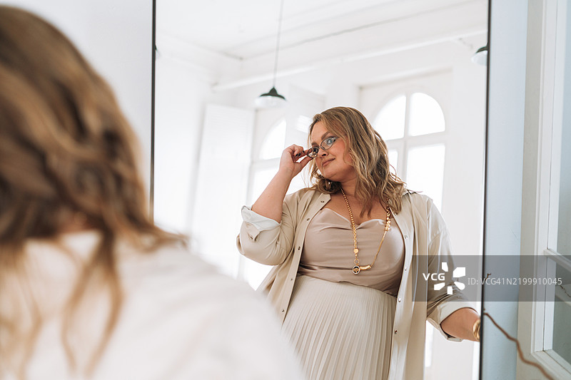 自信的年轻女性在镜子前欣赏自己，身材丰满。图片素材