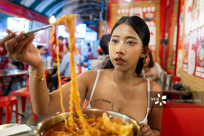 年轻女性在充满活力的餐厅环境中吃辣味拉面图片素材