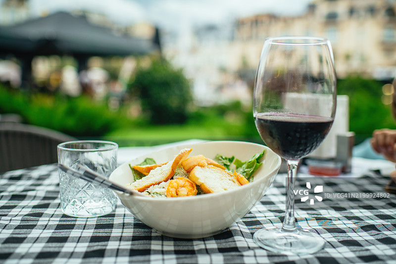 咖啡馆桌子上的凯撒沙拉配虾和一杯红酒图片素材