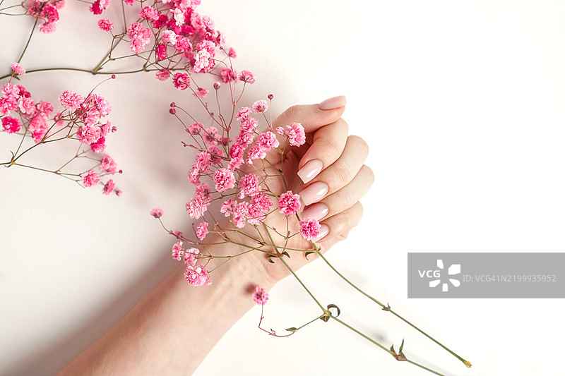 粉色美甲与白色背景上的花朵，俯视图。图片素材