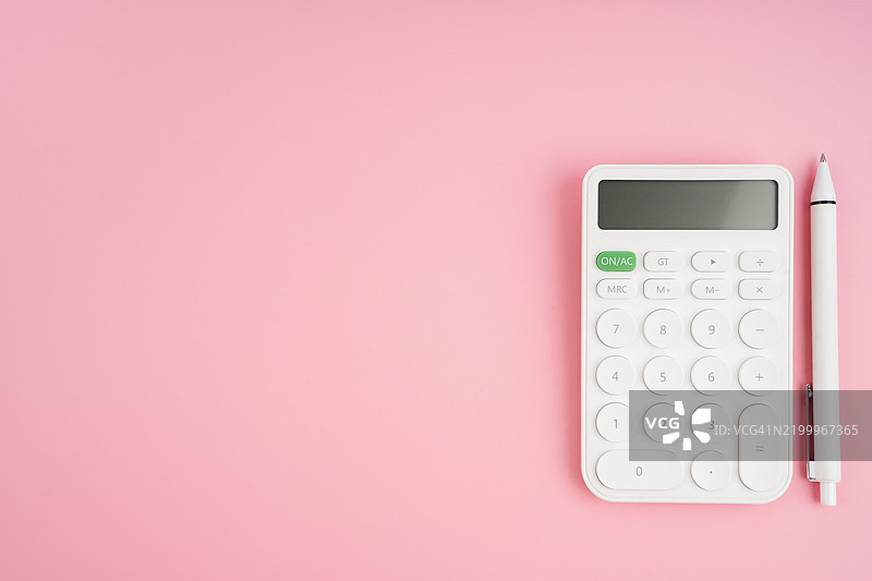 白色财务计算器和钢笔放在粉色背景上，留有空白空间。图片素材