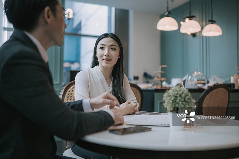 亚洲华裔美丽女性在咖啡馆里聆听她的经纪人讲解图片素材